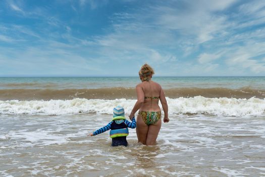 A woman and a child walk into the sea holding hands, view from the back. Family swimming in the sea