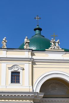 Green dome with a cross and a roof with sculptures against the blue sky. Fragment of the christian church