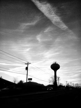 Image of Telephone pole and water tower silhouetted against a sunset sky in black and white
