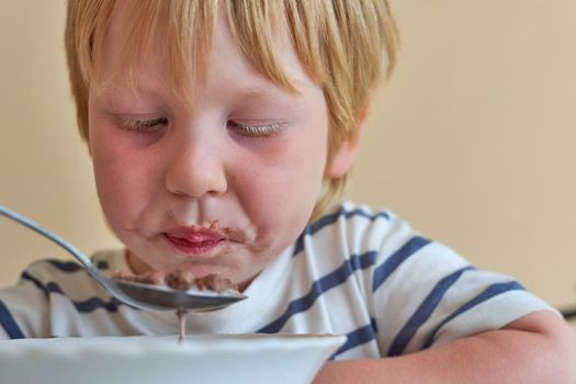 Little boy is having breakfast with chocolate balls with milk. Child eats dry breakfast with milk