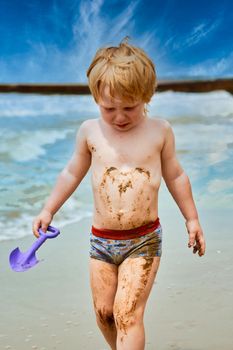 A little boy gets dirty in mud and walks crying along the beach along the sea