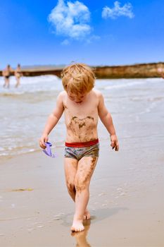 A little boy gets dirty in mud and walks crying along the beach along the sea