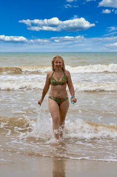 A woman in a swimsuit with white long hair comes out of the sea. Bathing blonde at the sea in summer