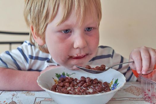 Little boy is having breakfast with chocolate balls with milk. Child eats dry breakfast with milk