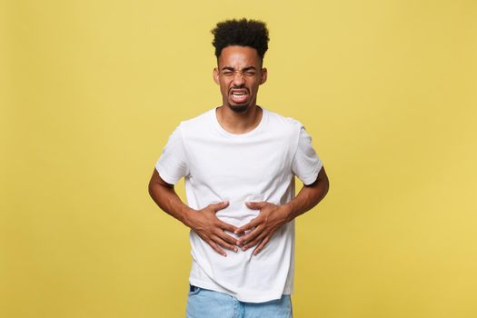 Closeup portrait of miserable, upset, young man, doubling over in stomach pain, looking very sick unwell, isolated on yellow background. Facial expressions emotion feelings, health issues.