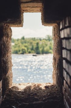 Observation window in the brick wall of the fortress for firing a gun with a view of the river water and the forest