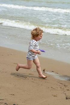 A little boy runs along the sandy beach along the seashore. Child resting on the sea
