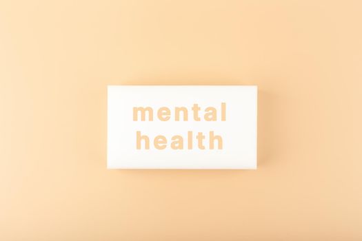 Creative minimal flat lay with white tablet with written mental health text on bright beige background. Concept of world mental health day, mental health assessment and awareness