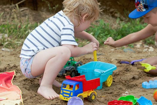 Two children play in the sand with plastic toys. Children playing in the sandbox