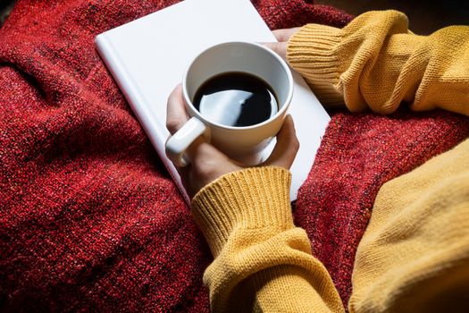 a woman with a red blanket on her legs relaxes by reading a book and enjoying a coffee
