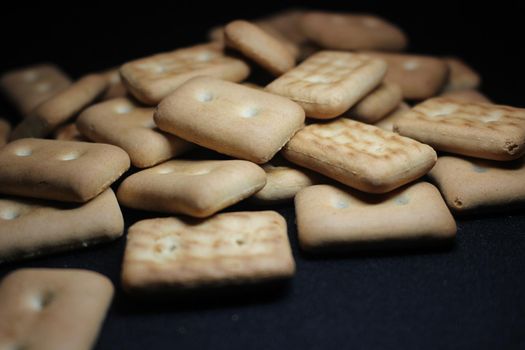 Close up top view of of biscuit cookies. Many rectangular biscuits with small pores on black floor