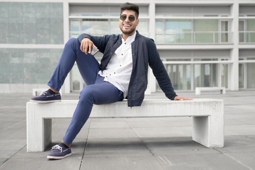 Portrait of young man in stylish sunglasses posing near modern building. High quality photo