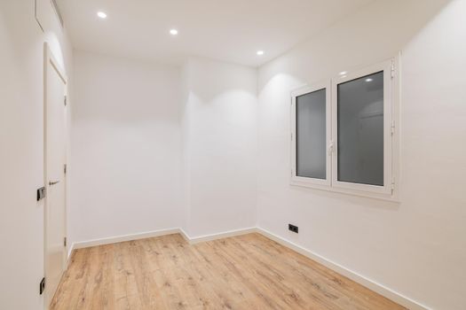 Empty clean room after renovation with white walls, window and wooden floor.