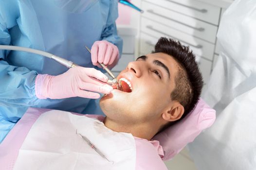 Young man having teeth examination at dentist office. Professional oral checkup in dentistry. Close up of female dentist working with dental tools in opened patient mouth. Stomatology and teeth care. High quality photo