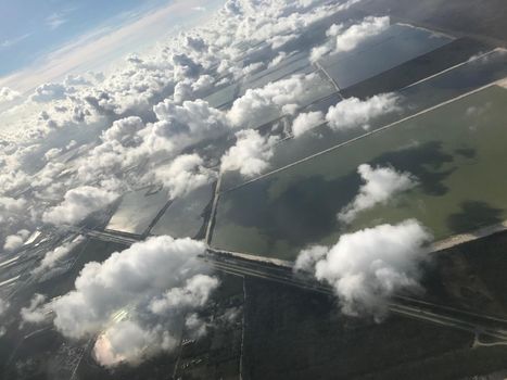 View from airplane window looking down on many clouds and farmland.