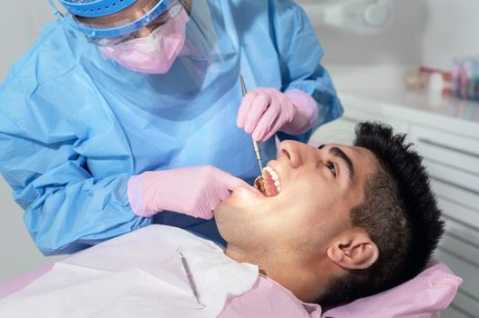 Young man having teeth examination at dentist office. Professional oral checkup in dentistry. Close up of female dentist working with dental tools in opened patient mouth. Stomatology and teeth care. High quality photo