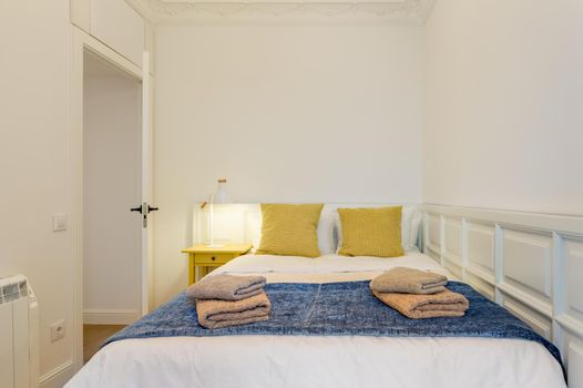 Interior of touristic bedroom. Yellow pillows on bed with towels. An apartment ready for booking by tourists.
