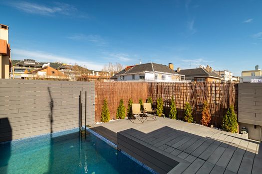 Private terrace on the roof of a house with swimming pool, sunbeds and wooden fence on sunny day in Barcelona