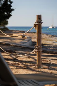 Wooden pole with ropes at the beach with view to sea and yacht. Calm atmosphere at the evening resort