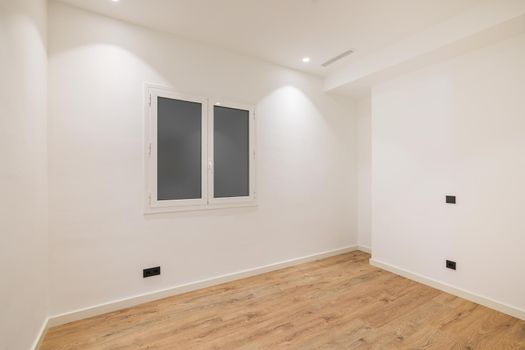 Empty clean room after renovation with white walls, window and wooden floor.