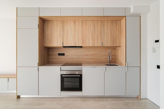 Contemporary minimal kitchen at empty refurbished apartment. Wooden furniture and modern appliances.
