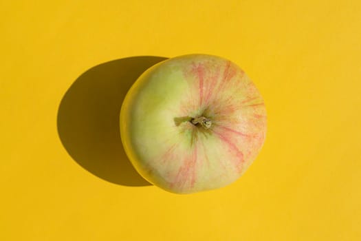 an apple with a hard shadow on a yellow background. High quality photo