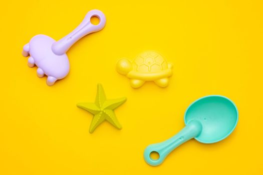 Plastic beach toy pastel color on yellow background. The development of fine motor concept. Creativity Game and summer concept top view