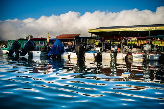 Artistic view of boats from the water with colorful water ripples and puffy clouds.