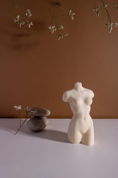 Candle in woman torso shape in brown interior with stone and dried flowers, autumn atmosphere vertical