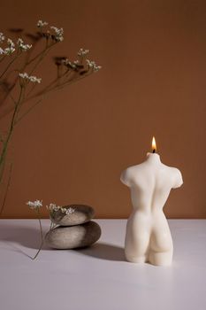 Candle in woman torso shape in brown interior with stone and dried flowers, autumn atmosphere vertical