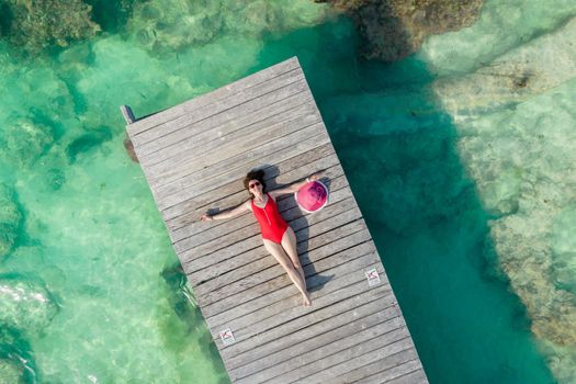 Aerial view of woman laying on wooden pier at sunny summer day in Cancun, Mexico, top view. Young sexy woman in red swimsuit in summertime in Caribbean. Summer beach vacation concept