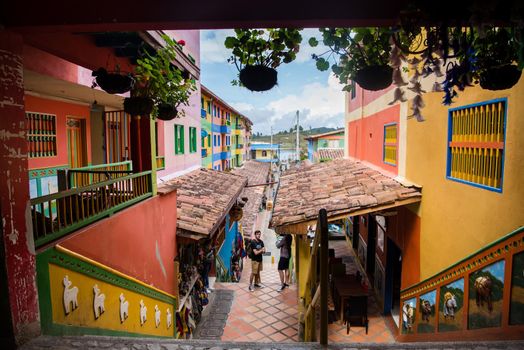 Wide view of downtown Guatape, Colombia with colorful patterns on the buildings and hanging potted flowers.