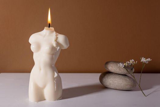 Candle in woman torso shape in brown interior with stone and dried flowers, autumn atmosphere vertical