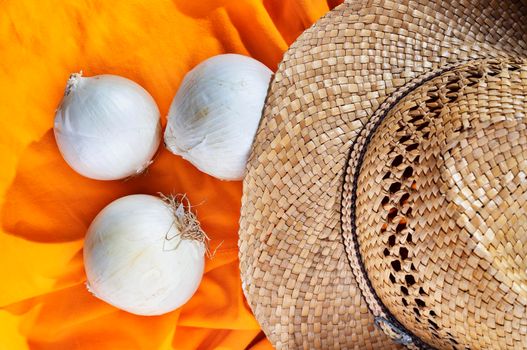 White onions or allium cepa on orange cotton background , beautiful  straw hat  