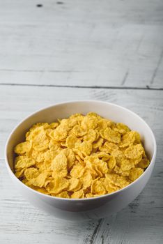 White bowl of corn flakes on a wooden surface