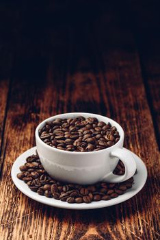 White cup full of roasted coffee beans on saucer