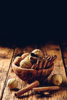 Cinnamon sticks and dried limes in wooden bowl on rustic table