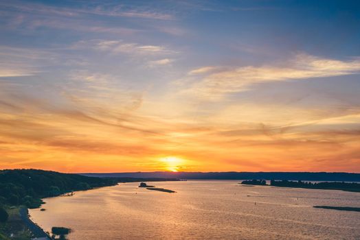 Summer sunset over the river shore with sky reflected on water