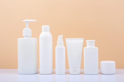 Set of white unbranded cosmetic bottles for face and body care in a row against bright beige background. Concept of organic, natural, eco friendly cosmetics and beauty products