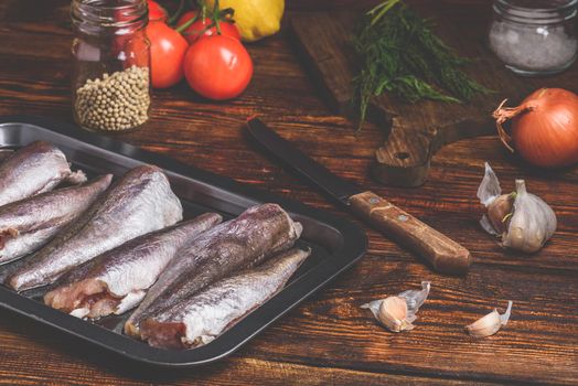 Hake carcasses on baking sheet with vegetables and spices