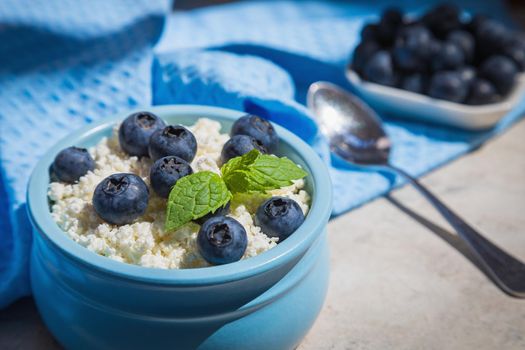 Morning fresh breakfast made from natural products from cottage cheese and blueberries. Nutritious cottage cheese and berries contain healthy vitamins. Blue background.