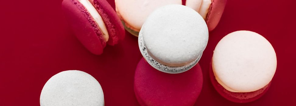 Pastry, bakery and branding concept - French macaroons on wine red background, parisian chic cafe dessert, sweet food and cake macaron for luxury confectionery brand, holiday backdrop design