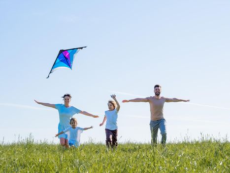 Parents and children running with kite on summer holiday vacation, perfect meadow and sky on seaside