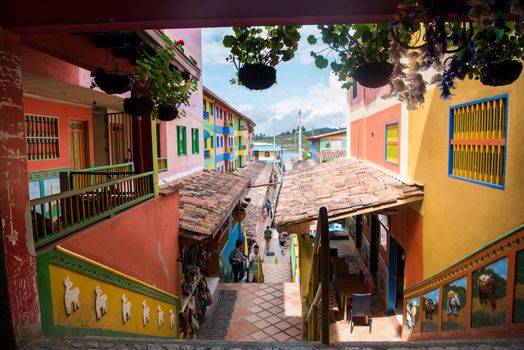 Wide view of downtown Guatape, Colombia with colorful patterns on the buildings and hanging potted flowers.