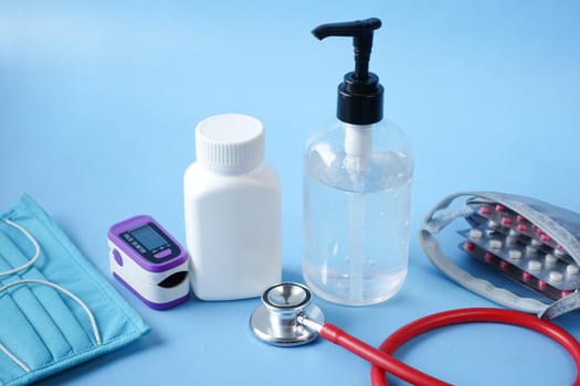 Surgical masks, thermometer and hand sanitizer on blue background .