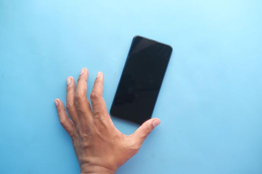 Close up of young man hand holding a smart phone on blue .