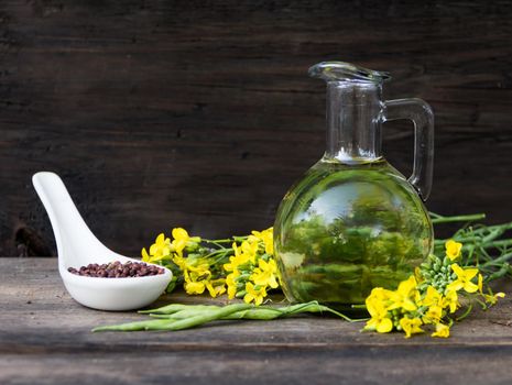 bottle rapeseed oil seeds and flowers on rustic wooden background