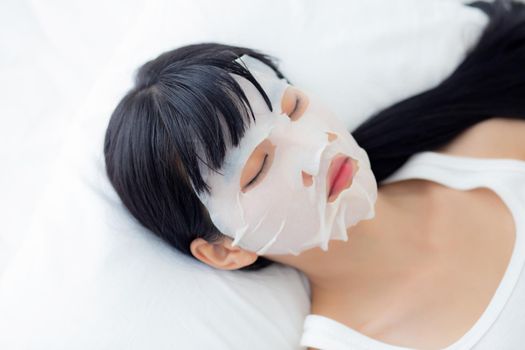 Beautiful young asian woman with sheet facial mask and sleep on bed at bedroom, beauty girl applying cosmetic and makeup with skin care face for wrinkle, skincare treatment, health and wellness.