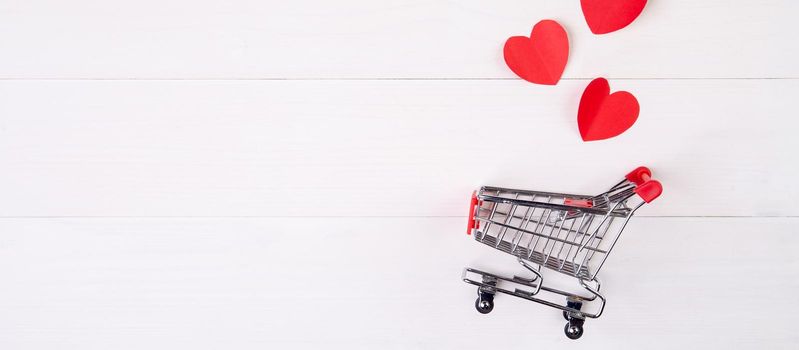 Shopping cart and heart shape paper on wooden table, sale concept in festive valentine day February 14, supermarket and store, symbol and celebration, commerce and selling in holiday concept.