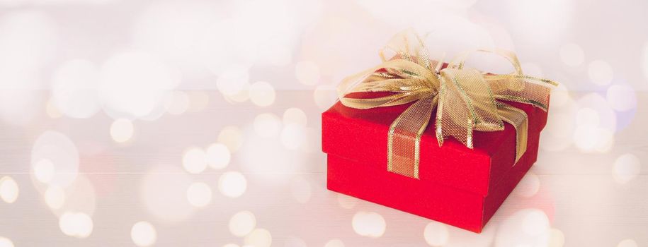 Red gift box on wooden table with bokeh background, love and romance, presents in celebration and anniversary with surprise on desk, happy birthday, copy space, nobody, valentine day concept.